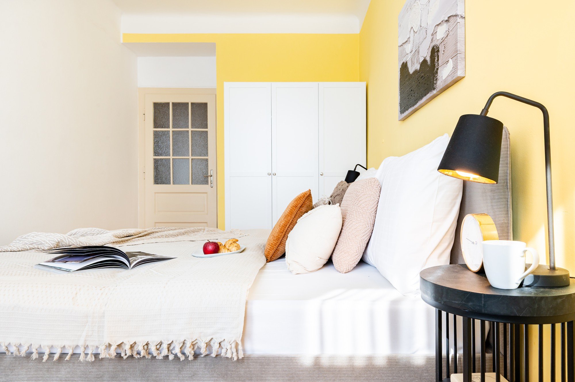 Erdvė yra gaivi, optimistiška ir harmoninga, su šiltais geltonais akcentais, sluoksniuota tekstile ir detalėmis, kurios miegamąjį paverčia jaukia, bet modernia vieta atsipalaiduoti.